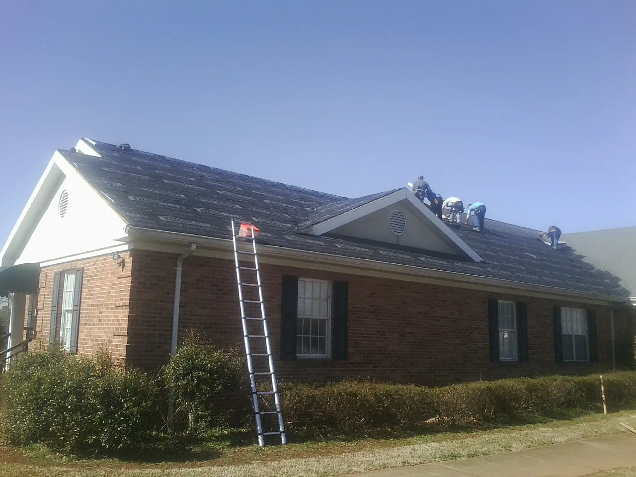 Crew tearing shingles off a brick ranch roof with a ladder set — Emergency Roof Repair work by our crew in Grandy