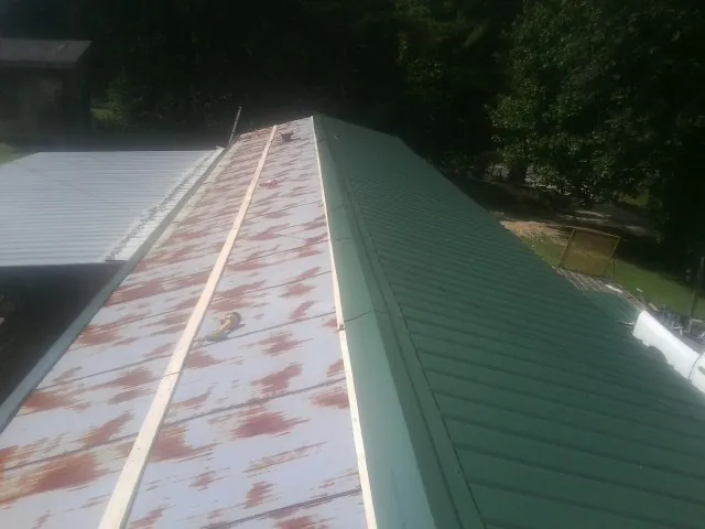 Old rusted panels beside newly installed green metal roofing — Wind Damage Roof Repair by Roofing Brothers in Grandy