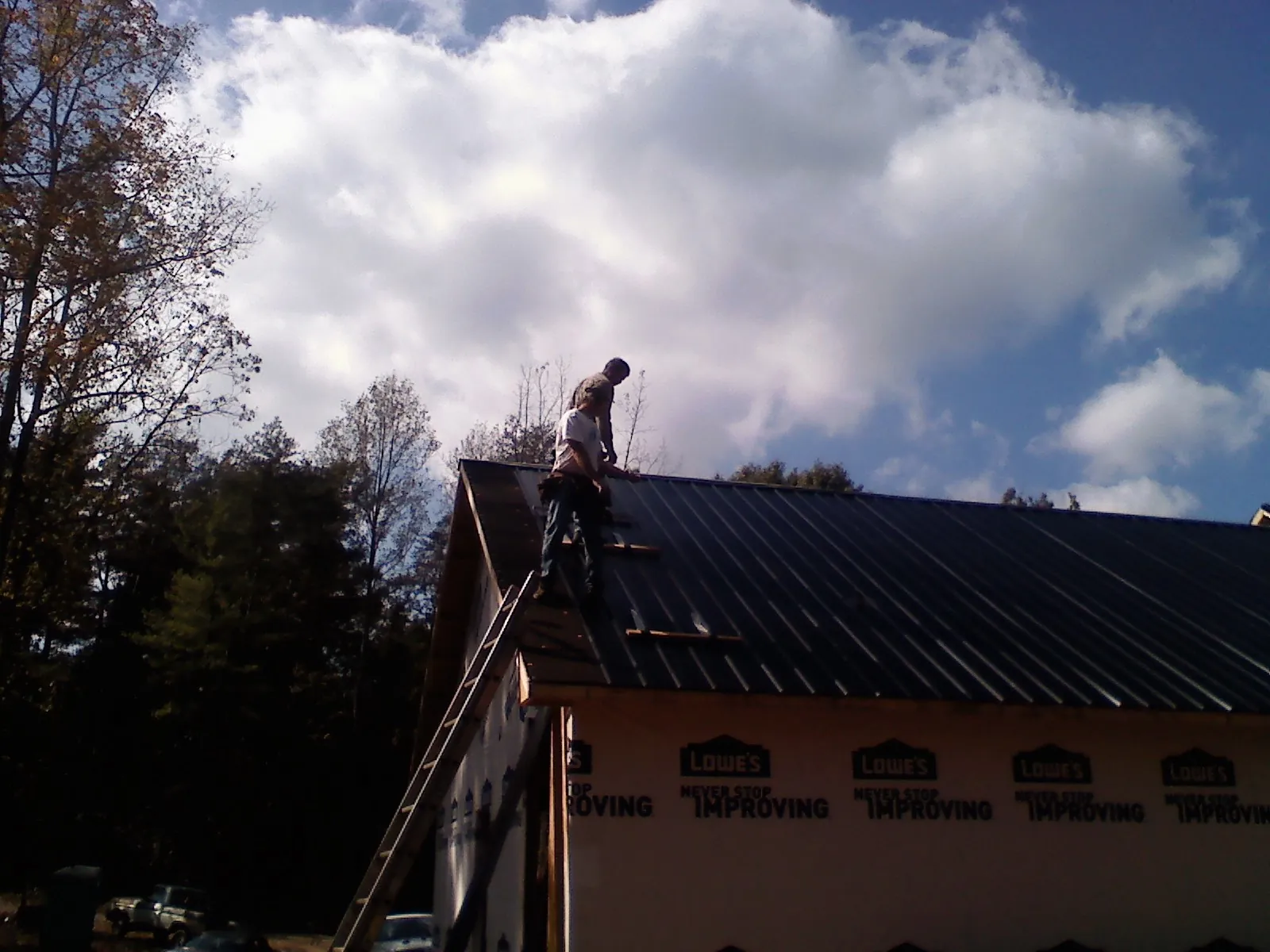Roofer fastening dark metal panels high against a cloudy sky, from a Roof Inspection job in Grandy