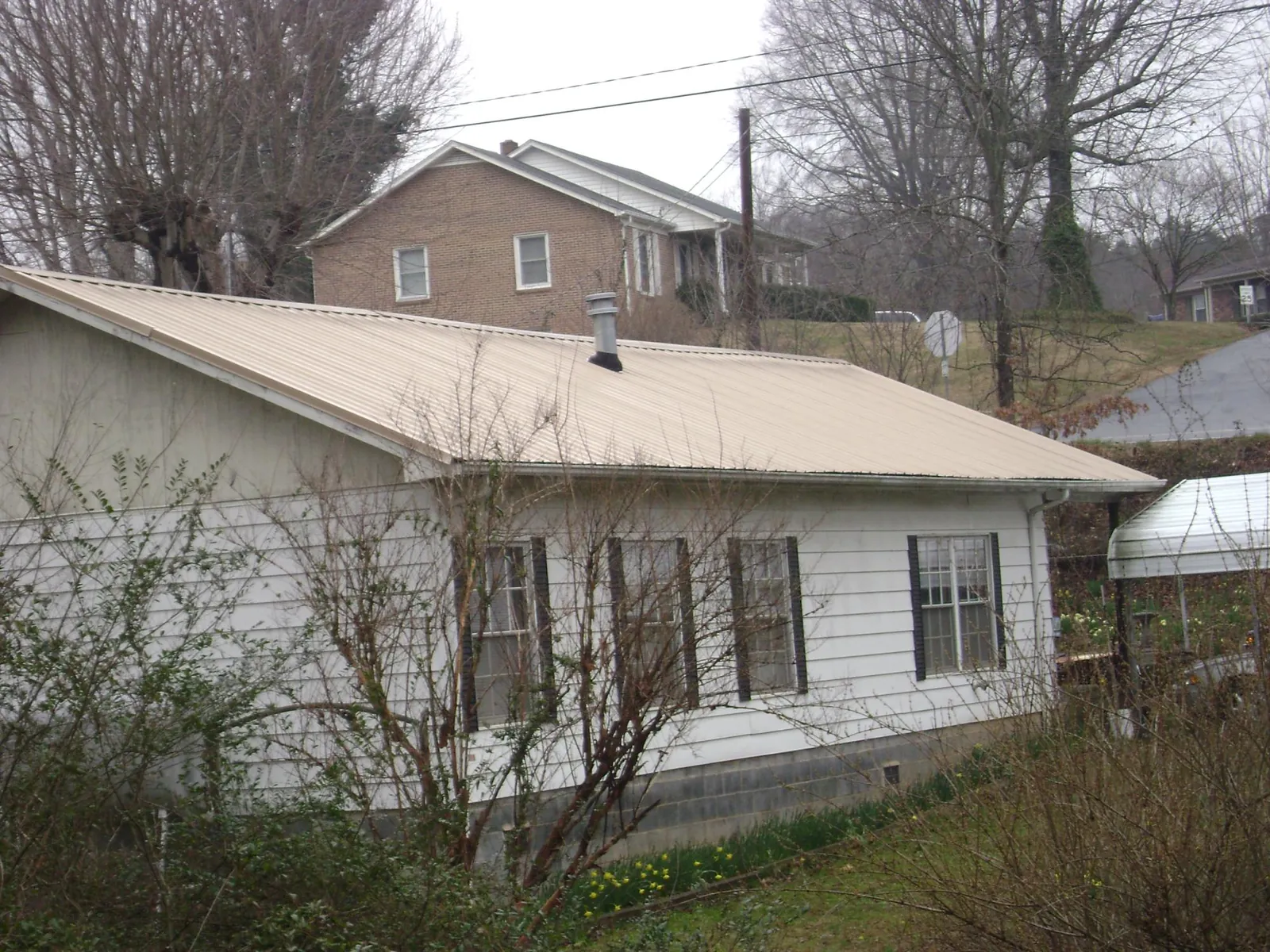Tan metal roof on a white sided house set into a hillside — Commercial Roofing by Roofing Brothers in Grandy